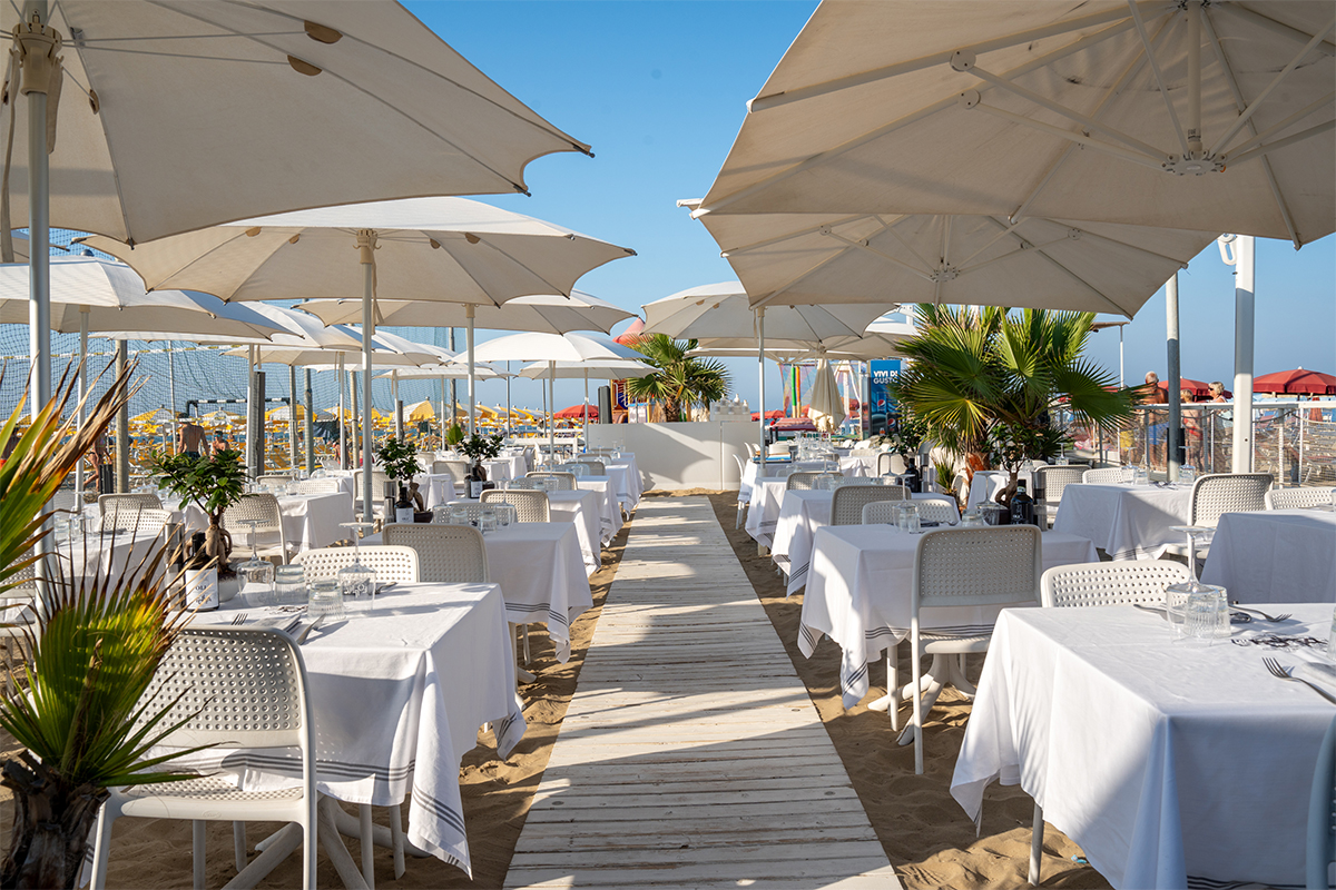Sala ristorante all’aperto sulla sabbia, con tavoli apparecchiati e ombrelloni