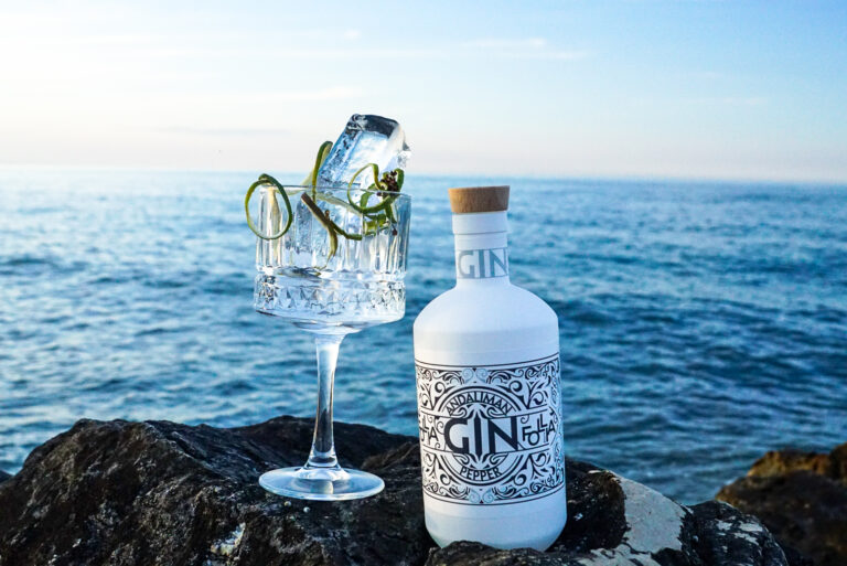 Bottiglia di Andaliman Pepper Gin Follia Beach con un Gin & Tonic davanti al mare