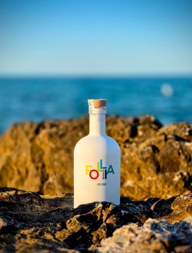Bottiglia bianca di Follia Beach Vodka sugli scogli davanti al mare